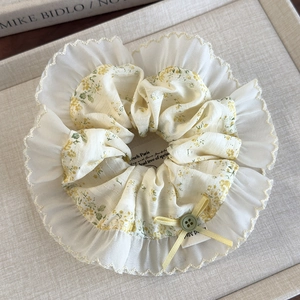 Detailed close-up of a floral hair scrunchie with lace trim and a bow on linen tray