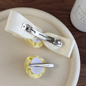Detail of yellow fabric rose and cream satin bow hair clips on a textured tray