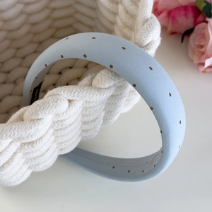 Gros plan d'un serre-tête bleu clair à pois en tissu épais sur un panier tressé blanc
