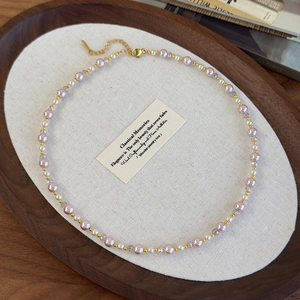 Gros plan d'un collier de perles roses et blanches avec perles dorées et fermoir mousqueton