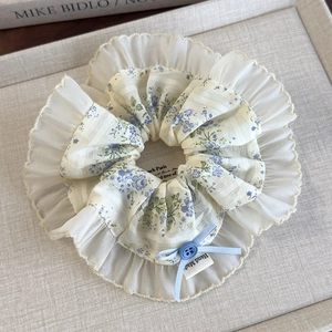 Detail of floral scrunchie with lace trim, blue bow, button, and handmade label