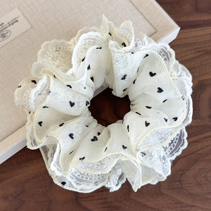 Close-up of cream mesh scrunchie with black heart patterns and delicate lace trim edge
