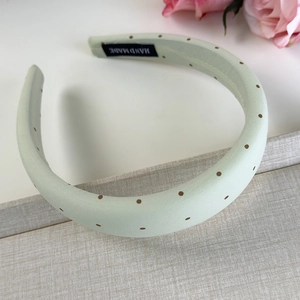 Détail d'un serre-tête vert clair à pois avec étiquette faite main et décor floral doux