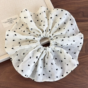 Detail of white mesh scrunchie with black heart prints on a minimalist wood background