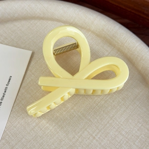 Détail d'une pince à cheveux en acrylique jaune crème au design croisé sur un plateau