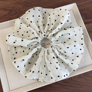Detailed view of white mesh scrunchie with black heart pattern on a display tray