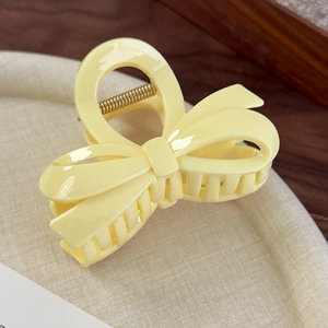 Gros plan d'une pince à cheveux nœud en acrylique jaune crème avec ressort en métal doré