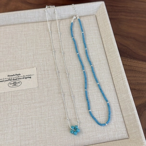 Détail du pendentif fleur bleue et du collier de perles turquoise sur plateau beige