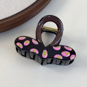 Dettaglio del fermaglio per capelli nero con pois rosa e verdi e molla in metallo oro