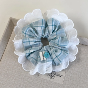Detailed macro view of checkered blue fabric hair scrunchie with lace trim and flower button