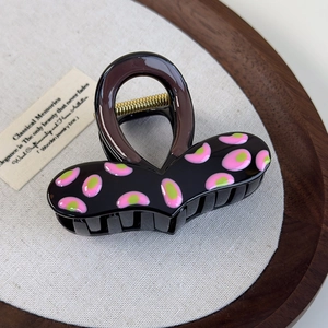 Dettaglio del fermaglio per capelli a cuore con smalto rosa e verde su base nera