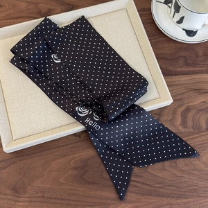 Detailed close-up of a black silk twilly scarf with white dots and rose patterns on a tray