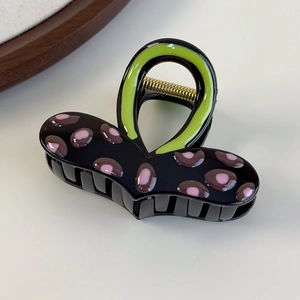 Dettaglio di un grande fermaglio per capelli nero e rosa maculato con manico verde