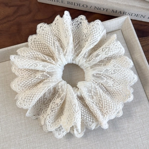 Détail d'un chouchou en dentelle beige avec broderie florale sur un plateau en tissu doux