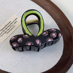 Dettaglio di un fermaglio a cuore nero e verde con motivo leopardato su un vassoio di legno