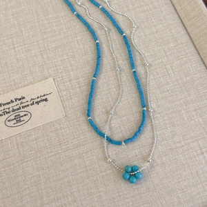 Collier double épaisseur avec perles bleues et pendentif fleur sur fond en lin beige