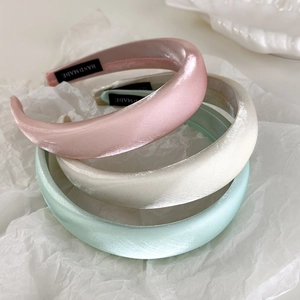 Detailed macro view of three satin padded headbands in pink, cream, and mint green colors