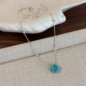 Détail du pendentif fleur perlé bleu sur chaîne argentée posé sur une assiette coquillage