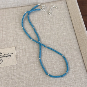 Détail de perles cylindriques bleues et d'espaceurs en métal argenté sur collier perlé
