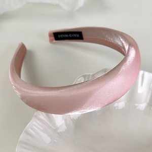 Detailed macro shot of pink satin headband with hand made tag on white ceramic plate