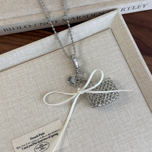 Detail of silver beaded chain necklace with hollow mesh pendant and white leather bow