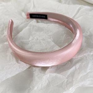 Detailed close-up of pink satin headband showing the handmade label and silk texture