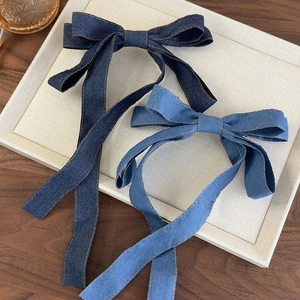 Close-up of denim bow hair clips with yellow stitching on a beige display tray