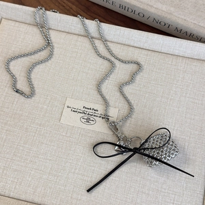 Detail of silver bead chain necklace featuring a black bow and mesh bag pendant