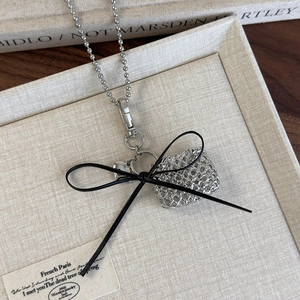 Detailed macro view of silver hollow bag pendant with black ribbon bow on a long chain