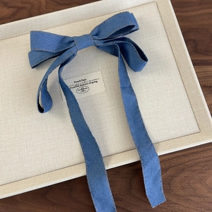 Detail view of denim blue bow hair clip with orange stitching and long ribbons