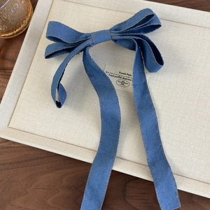 Close-up of denim bow hair clip with yellow stitching and long ribbons on display