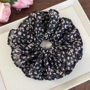 Gros plan sur un chouchou en mousseline à fleurs roses sur fond en tissu noir