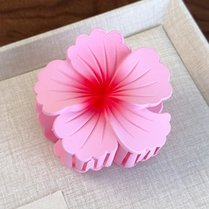 Close-up of a matte pink floral hair claw clip with dark red gradient details