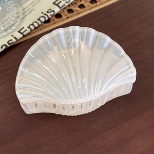 Detail of seashell-shaped hair claw clip in iridescent creamy white with acetate texture
