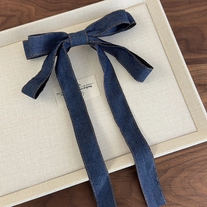 Detail of denim bow hair clip with orange contrast stitching and long flowing ribbons