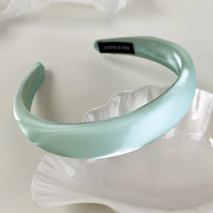 Detail of mint green satin padded headband showing smooth texture and handmade label