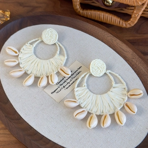 Macro view of bohemian round woven raffia earrings with natural seashell charms