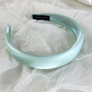 Detail of mint green satin sponge headband featuring a black handmade woven label