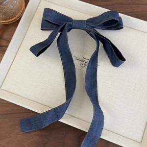 Close-up of a blue denim bow hair clip with vintage orange stitching and long streamers