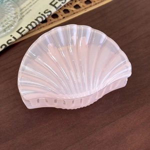 Macro shot of pearlescent light pink shell-shaped hair claw clip on wooden table