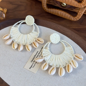 Detail of bohemian raffia woven hoop earrings with natural cowrie shell pendants