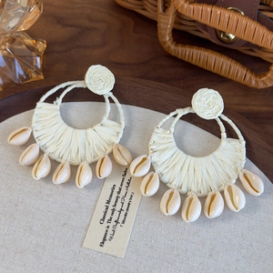 Close-up of bohemian raffia woven earrings with natural cowrie shells on rustic background