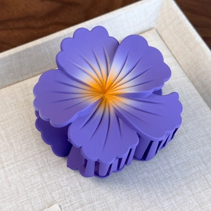 Detail shot of a matte purple floral hair claw clip with yellow gradient center on fabric