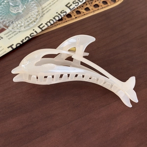Macro detail of a pearl cream dolphin hair claw clip with glossy finish and metal spring