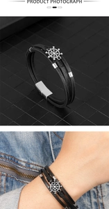 Detail eines mehrlagigen schwarzen Lederarmbands mit silbernem Steuerrad und Magnetverschluss