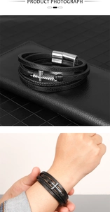 Detail showing multilayered black woven leather bracelet with a silver metal cross and magnetic clasp