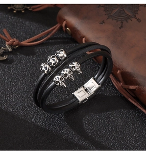 Macro detail of multi-layer leather bracelet featuring vintage silver skull charms and buckle