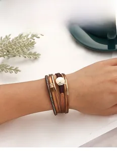 Detail of bohemian multilayer leather bracelet featuring a golden metal disc and magnetic clasp