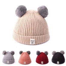 Detail view of colorful knitted baby hats with double faux fur pom-poms and retro label