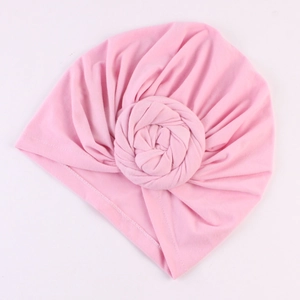 Détail d'un bonnet turban rose avec design plissé et décoration de fleur en tissu